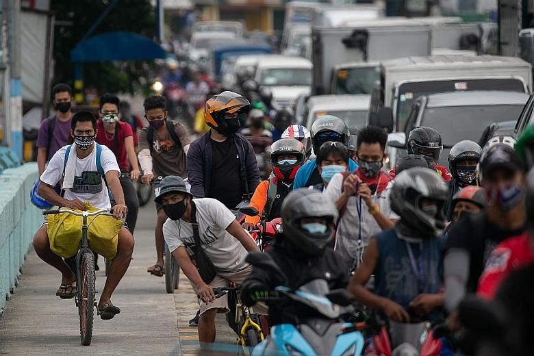 Cyclists riding on the sidewalk as traffic built up at a checkpoint in Marikina city in Metro Manila yesterday, the first day of a stricter lockdown to curb coronavirus infections in the Philippines. PHOTO: REUTERS A Philippine soldier checking the d