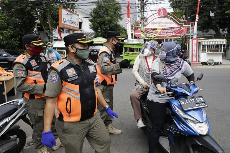 Police officers talking to motorcyclists during a mask-wearing and public health protocols campaign at a checkpoint in Jakarta yesterday. The Indonesian government plans to distribute social aid packages that include face masks and educate the public
