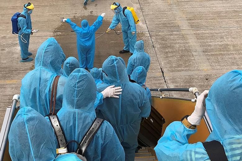HONG KONG: Temperature screening outside a Hong Kong wet market on Friday. VIETNAM: Healthcare workers (left) spraying disinfectant at Vietnamese nationals after their Covid-19 repatriation flight landed at Can Tho Airport in the Mekong Delta region 