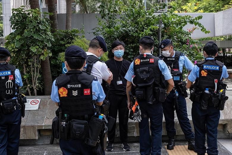 Police officers questioning a man wearing press credentials in the vicinity of a planned lunchtime protest in Central district in Hong Kong yesterday. A national security unit has been formed to handle sensitive visa applications, such as those from 