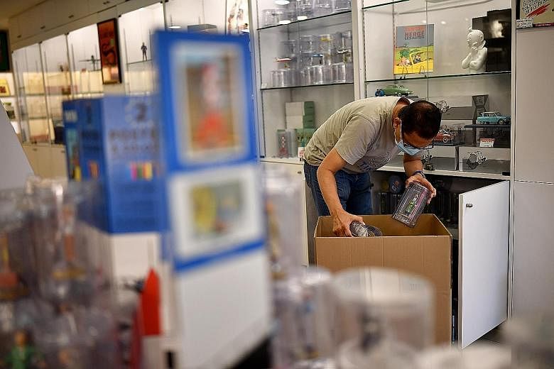 A Tintin Shop worker packing up as the business prepares to close for good at the end of the month. Souvenir shops in Chinatown have taken a massive hit from coronavirus-related travel curbs. Above: Ms Cindy Zhao (in blue) moving her goods, with the 