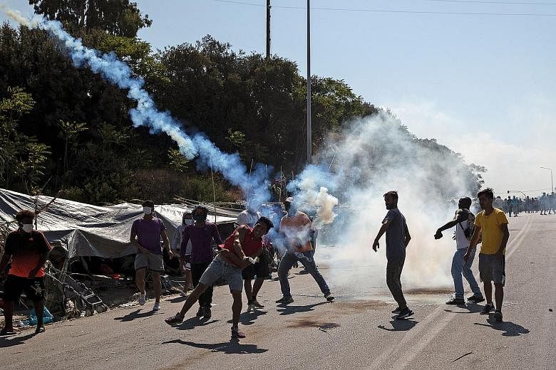 A migrant woman and children shouting in fear (left) after police threw tear gas during clashes yesterday near the city of Mytilene on the Greek island of Lesbos, a few days after fires destroyed the Moria refugee camp. Migrants throwing stones (belo