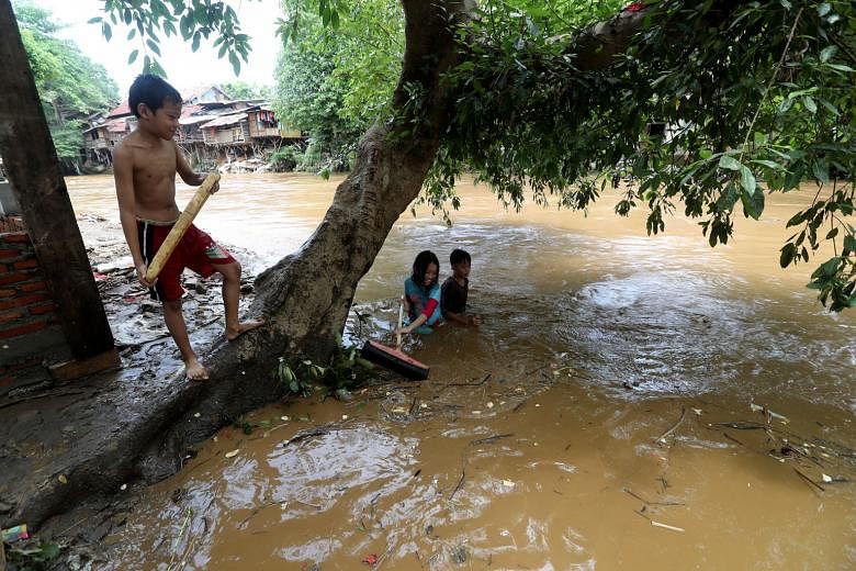 Left: A car swept away by floodwaters ending on top of debris in Pesawahan village in Sukabumi, West Java, yesterday. Below: Trash scrapers cleaning a dirty river (left) and children playing in it (right) yesterday after flash floods and landslides s