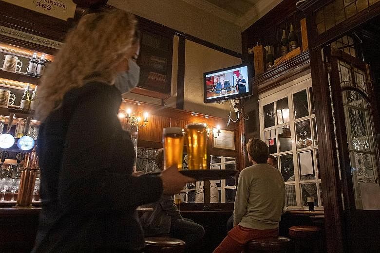 Patrons at a London pub watching British Prime Minister Boris Johnson addressing the nation about the latest updates on the country's Covid-19 restrictions on Tuesday. The measures, starting today, entail an extension of the mandatory use of face mas