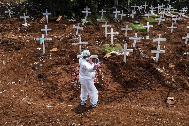 Photojournalist Muhammad Adimaja wearing a custom stencilled face mask with words that loosely translate as "virus protector". Right: A family member in a protective suit taking a picture at the grave of a Covid-19 victim in Pondok Rangon cemetery in
