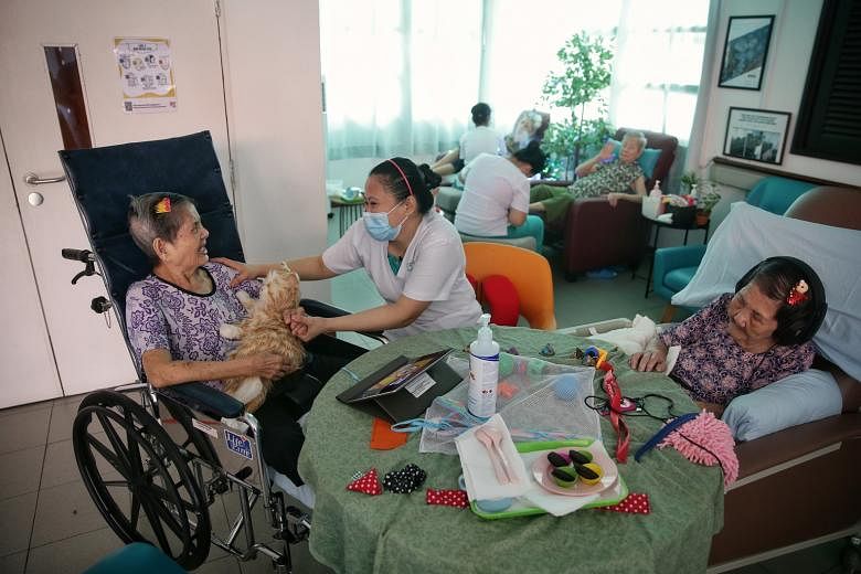 Madam Tang Nyuk Lin (left, with an interactive toy cat) and Madam Khoo Chui York (right, wearing headphones) at Apex Harmony Lodge. The home, which cares for dementia patients, is rolling out a project called Namaste Care, which among other things gi