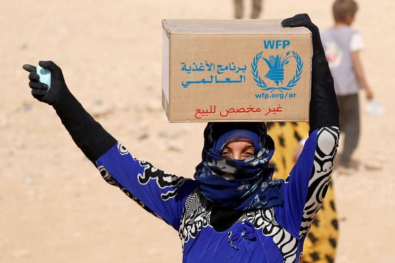 A 2017 photo showing a woman at a refugee camp in Syria holding a food stamp and carrying a box of food aid given by the United Nations' World Food Programme. 