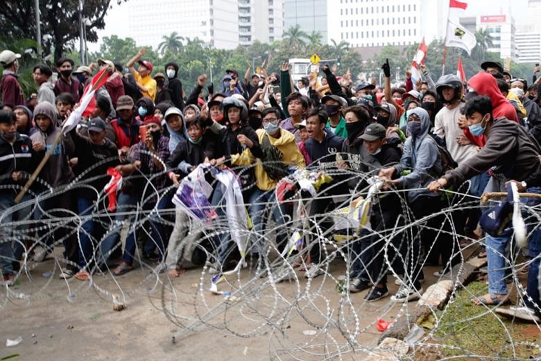 Above: Protesters in Jakarta trying to remove barbed wire during a rally against Indonesia's new job law yesterday. 