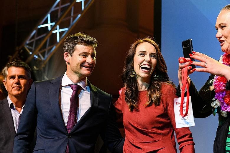 Above: New Zealand opposition leader Judith Collins congratulated Prime Minister Jacinda Ardern (right, in red) on an "outstanding" result yesterday. Right: Ms Ardern with her partner Clarke Gayford at Auckland Town Hall last night. She said Labour's