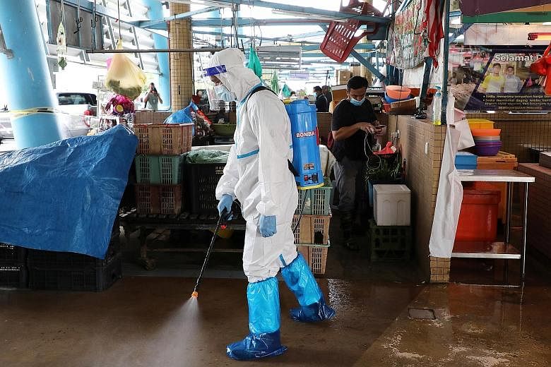 Above: A worker wearing personal protective equipment spraying disinfectant at a market in Putrajaya, Malaysia, last Thursday. Left: Some stores in Malaysia's iconic Suria KLCC shopping mall are closing earlier than usual as customers stay home amid 