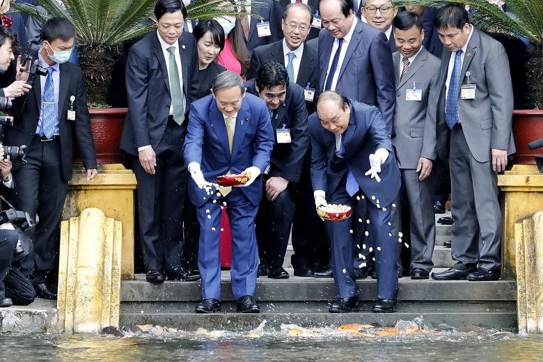 Japanese Prime Minister Yoshihide Suga (front row, left), on his first foreign trip since taking office, and his Vietnamese counterpart Nguyen Xuan Phuc feeding fish at the Presidential Palace compound in Hanoi yesterday. The two leaders stressed the