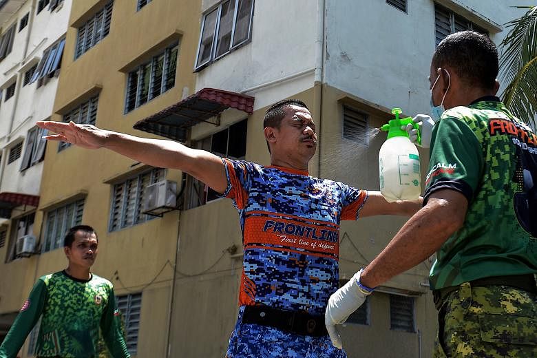 Members of Malaysia's Civil Defence Force and People's Volunteer Corps being sprayed with disinfectant after distributing food to hostel occupants in Kuala Lumpur yesterday. The government allowed mosques, gyms and parks to reopen, just days after an