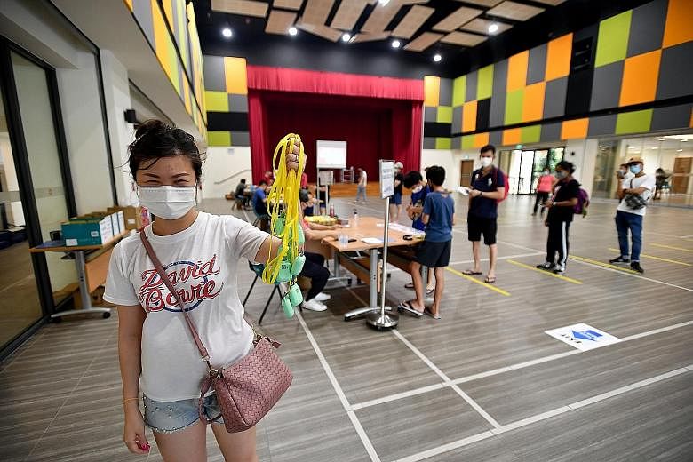 Sales manager Ho Kai Peng collecting seven TraceTogether tokens for her family at Teck Ghee Community Club in Ang Mo Kio yesterday. Those collecting the tokens are also given a magnetic information guide explaining how to use the device, which comes 