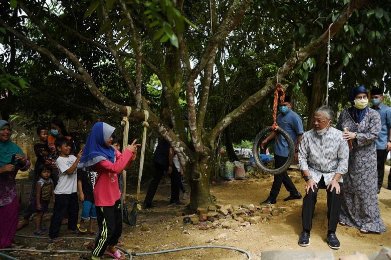 Sultan Abdullah and his wife, Tunku Azizah Aminah Maimunah Iskandariah, with villagers in Pahang in June. With Malaysia's ethnic Malay community divided like never before, the King is being dragged into the fray to play the central role of adjudicato