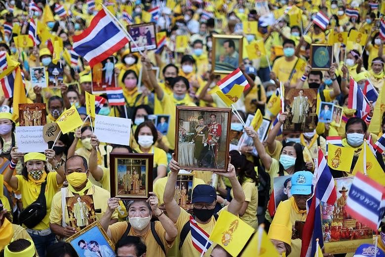 Royalists wearing yellow shirts at an event to support the monarchy in Bangkok on Tuesday. One of them held up a picture of the late King Bhumibol Adulyadej. PHOTO: REUTERS Pro-democracy demonstrators showing the three-finger anti-government salute d