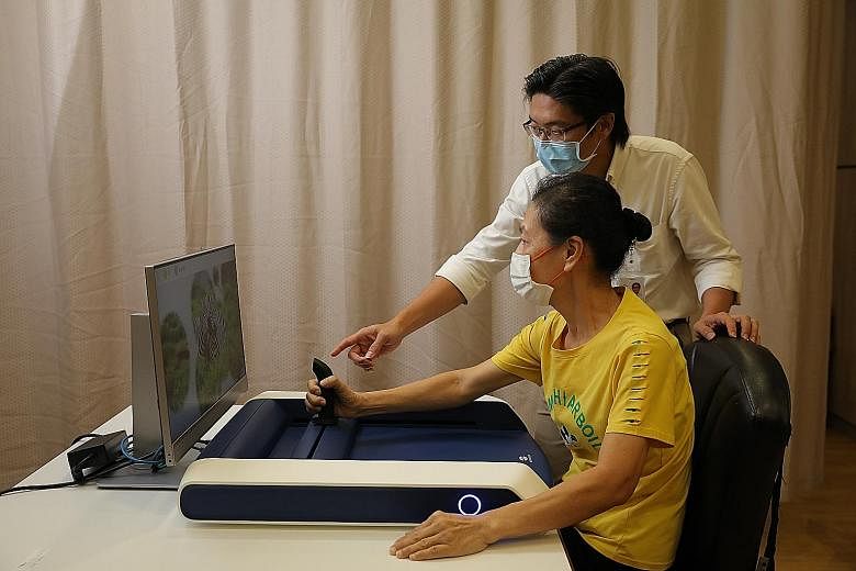 Madam Seet Jeu Luang, 60, who had a stroke in July last year, using the H-Man device yesterday during a media demonstration, under the guidance of Mr Christopher Kuah, principal occupational therapist at Tan Tock Seng Hospital. Madam Seet was one of 