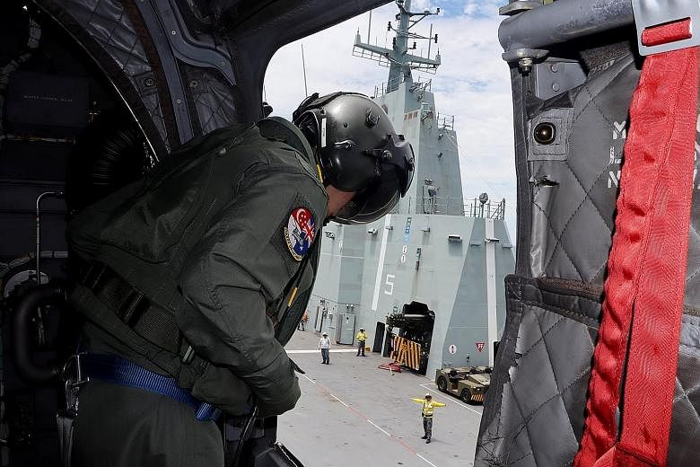 A Republic of Singapore Air Force air crew specialist (left) on board the CH-47D Chinook keeping a lookout for blind spots during the helicopter's landing on the HMAS Adelaide (above) in the waters off Townsville in Queensland, Australia, last Saturd