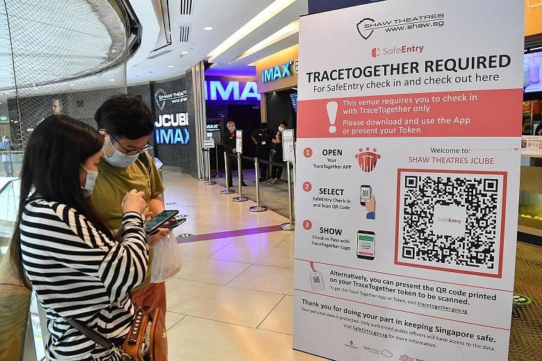 Cinemagoers Sophia Soo (foreground) and Chin Zhi Yu downloading the TraceTogether app to check in before entering Shaw Theatres at JCube mall yesterday. From Nov 16, using the TraceTogether app or token will be the only way to check in for SafeEntry 