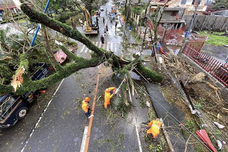 A toppled electric post in Tigaon. Power was knocked out in areas battered by fierce winds, including some large cities in metropolitan Manila. Workers clearing a toppled tree in the typhoon-hit town of Tigaon in Camarines Sur province yesterday. Typ