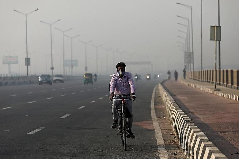 A masked cyclist riding along a highway on a smoggy morning in New Delhi last Friday. Coronavirus cases and air pollution are spiking across major cities in India, including New Delhi, one of the worst-affected areas for smog from rural burning. PHOT