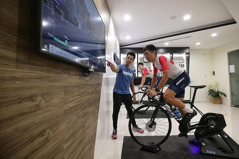 National cyclists Darren Lim (front), 22, and Samuel Leong, 19, on the indoor smart trainer last month as Garmin community manager Edwin Shen introduces the features of the system.
