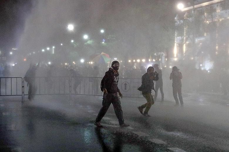 Protesters getting soaked after police deployed water cannon during a march to the Grand Palace in Bangkok yesterday. Demonstrators hauled along mock mailboxes for people to stuff letters to King Maha Vajiralongkorn.