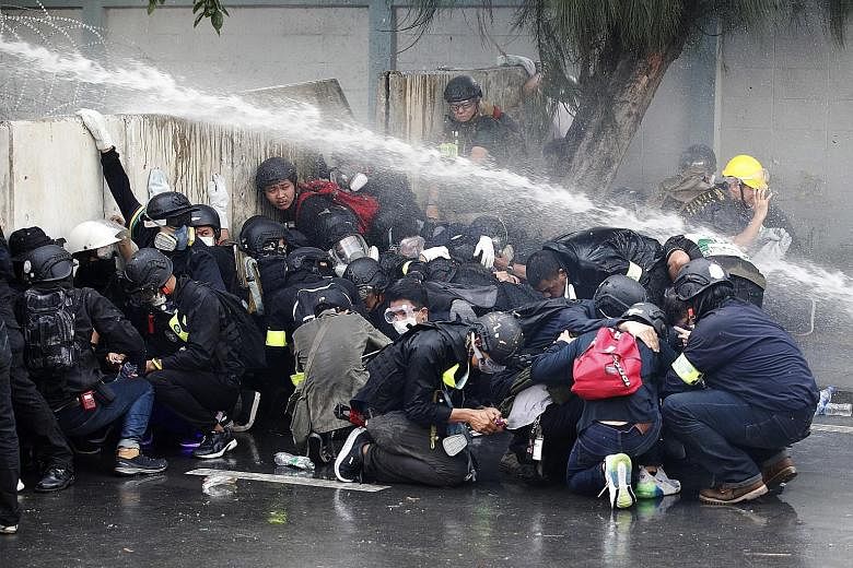 Thai pro-democracy protesters taking cover as police fire tear gas and water cannon at them during a demonstration calling for constitutional changes in Bangkok yesterday. Thai police using water cannon with chemical-laced water to disperse pro-democ
