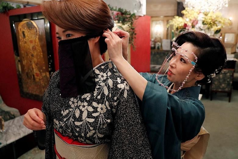 A bar hostess helping another to wear a "face veil mask" at a club in Tokyo on Monday. Japanese kimono maker Otoduki, which invented the mask, said it was inspired by the cloth masks worn by belly dancers, and it helps hostesses, dancers and musician