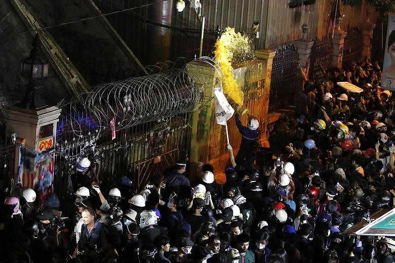 A pro-democracy protester throwing a bucket of paint over the gate of the Thai police headquarters during a demonstration calling for political and monarchy reform in Bangkok on Wednesday. Protesters said this was a response to the use of water canno