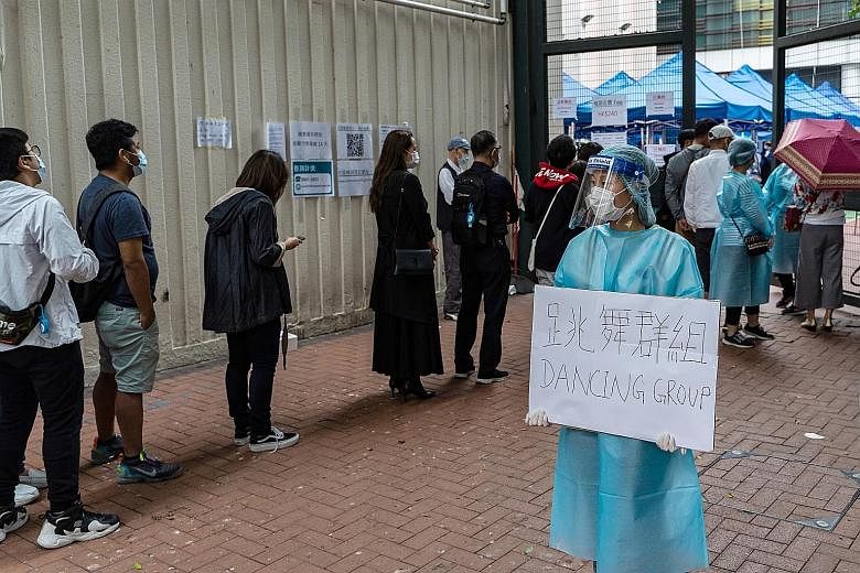 A healthcare worker holding a sign referring to a dance studio cluster, as people waited outside a community testing centre in Hong Kong on Monday. The government yesterday issued a notice to say that seven more venues across the city had been added 