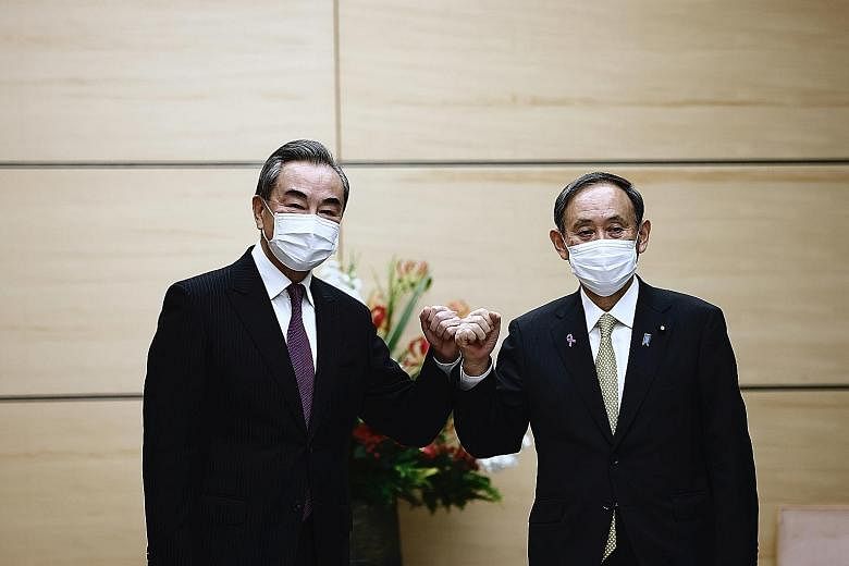 Japanese Prime Minister Yoshihide Suga (at right) bumping fists with China's Foreign Minister Wang Yi at the start of their meeting in Tokyo yesterday. It was Mr Suga's first high-level meeting with a senior Chinese official since he was elected as J