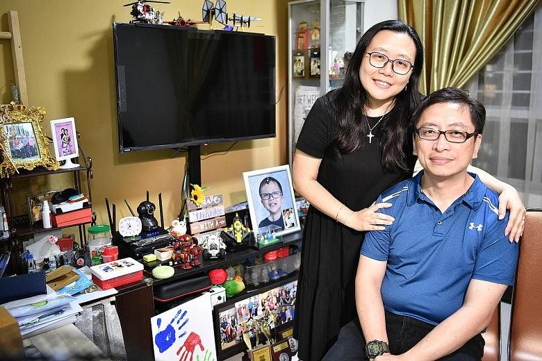 Raphael's parents, Mr William Lee, 47, a course manager with St John Singapore, and Mrs Winnie Lee, 45, a former childcare teacher who left her job last year to look after her son, beside the TV console that's crowded with Raphael's belongings. The b