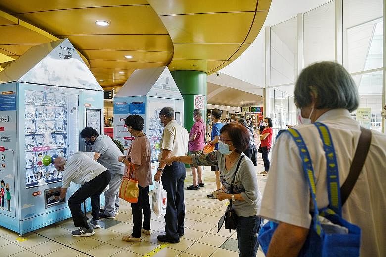 People collecting new reusable face masks at a vending machine in the Toa Payoh Bus Interchange on the first day of distribution by Temasek Foundation yesterday. Each person is entitled to one free mask kit, which contains a pair of reusable masks an