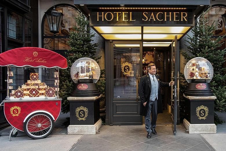 (Above) A collection of small Sacher Torte cakes. (Left) Concierge Uwe Kotzendorfer at the entrance of Hotel Sacher in Vienna on Nov 25.