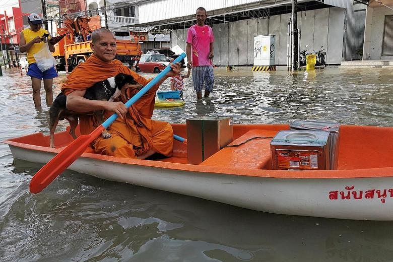 Above: A Buddhist monk paddling down a flooded street in Thailand's Nakhon Si Thammarat province yesterday. Right: Thai security forces carrying pigs from a flooded farm in the southern province of Surat Thani. PHOTOS: REUTERS, AGENCE FRANCE-PRESSE