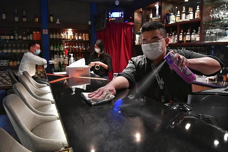 A worker cleaning the bar counter at Bell Bar in Cuppage Plaza as it opened for business last night. It is among three establishments allowed to reopen for two months under the small-scale pilot programme, with strict safe management measures in plac