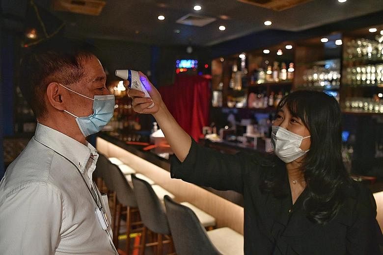 Cuppage Plaza's Bell Bar owner Mabel, who wanted to be known by only one name, taking the temperature of customer Fujita Koichi yesterday. ST PHOTO: CHONG JUN LIANG