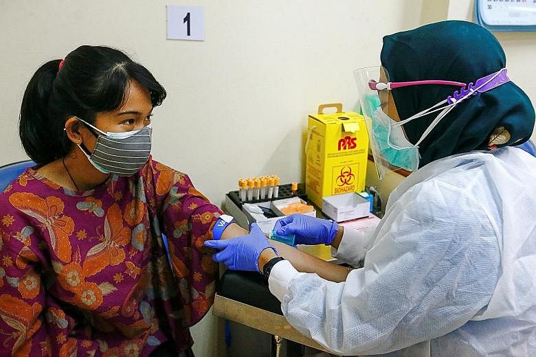 Above: A staff member taking a woman's blood sample for Covid-19 serological testing at a Jakarta hospital last week. PHOTO: REUTERS Left: An advertisement for coronavirus testing in Bandung, West Java. Indonesia is gearing up to roll out its vaccina
