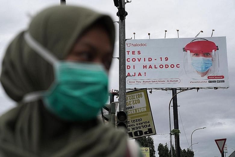 Above: A staff member taking a woman's blood sample for Covid-19 serological testing at a Jakarta hospital last week. PHOTO: REUTERS Left: An advertisement for coronavirus testing in Bandung, West Java. Indonesia is gearing up to roll out its vaccina