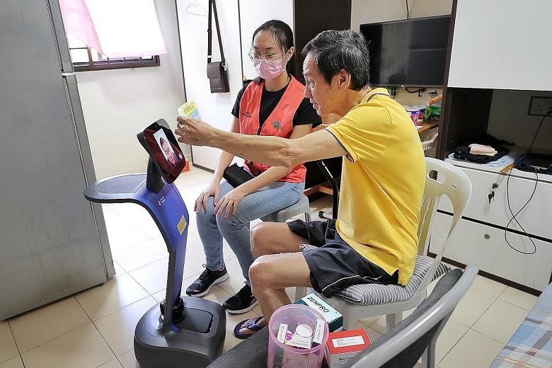 Mr Ow Soo Tian, 71, speaking to Alexandra Hospital pharmacist Joshua Low in a teleconferencing session enabled by the hospital's smart robot Temi, in Mr Ow's one-room flat in Mei Ling Street on Tuesday. He is assisted by Alexandra Hospital volunteer 