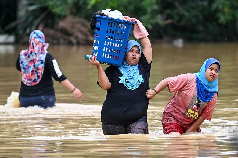 Several residents, one carrying her belongings, wading through floodwaters in Kuala Kaung, near Lanchang in Malaysia's Pahang state, yesterday. The number of people displaced during Malaysia's annual monsoon season, which runs from November to March,