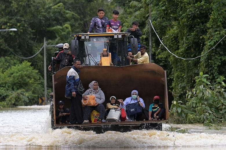 Above: Flood-hit Pahang residents being evacuated to safety in a digger yesterday. Left: Some others swimming through floodwaters in the eastern Malaysian state. PHOTOS: AGENCE FRANCE-PRESSE