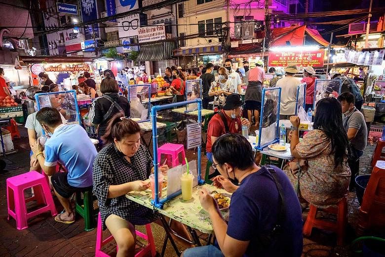 Diners separated by screen dividers at a street food corner in Bangkok on Sunday. Thailand, battling its second wave of coronavirus infections, has imposed an array of restrictions that vary depending on which provincial border one crosses, with the 