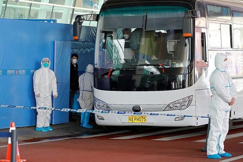 Members of the World Health Organisation team boarding a cordoned-off bus that was guarded by half a dozen security staff in full protective gear at the airport in Wuhan yesterday.