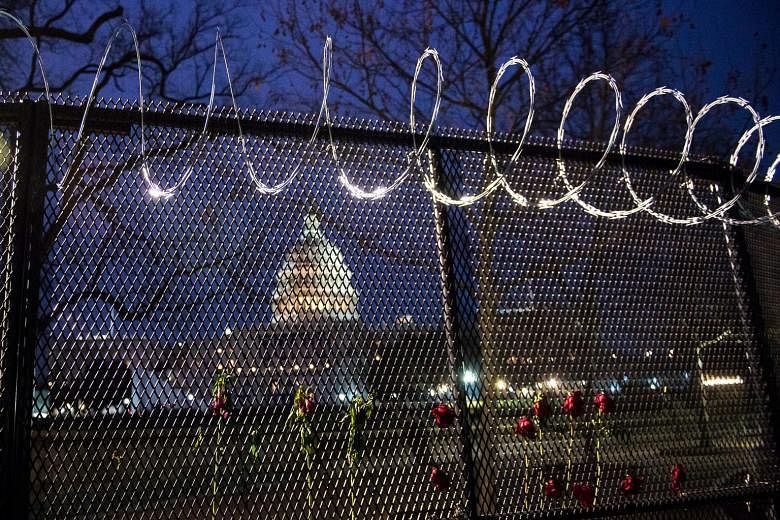 Flowers placed along the razor wire fencing that now surrounds the US Capitol in Washington on Friday. Across the country, too, tall chain-link fences have been erected around state capitals.