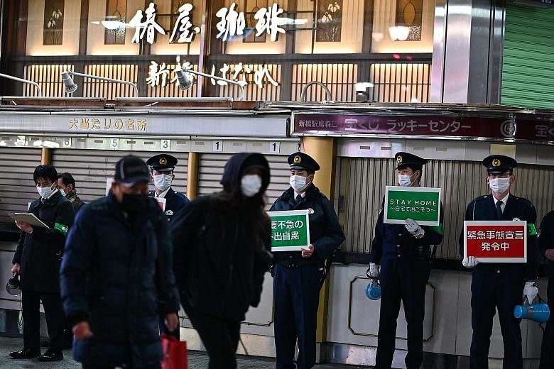 Policemen in Tokyo holding signs last Friday asking people to stay home amid the coronavirus outbreak in the Japanese capital. The seven-day moving average in Tokyo stood at 1,202 cases in the week ending Sunday - down from 1,765 cases in the week of