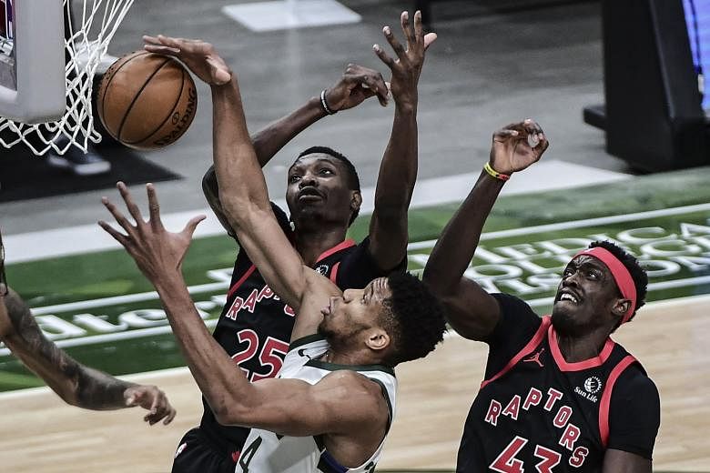 Milwaukee Bucks forward Giannis Antetokounmpo reaching for a rebound against Toronto Raptors forwards Chris Boucher and Pascal Siakam (No. 43) in the first quarter of their NBA game at Fiserv Forum. The Bucks lost 124-113 and have now suffered their 