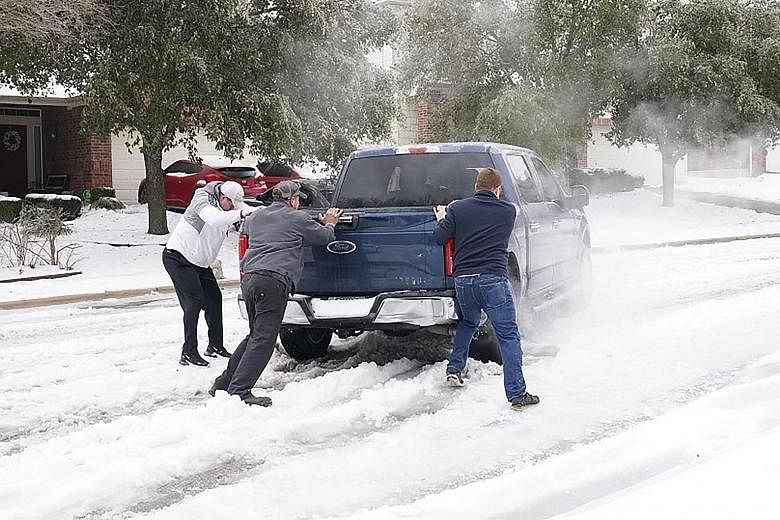 Residents helping a pickup driver to get out of ice on the road in Round Rock, Texas, on Wednesday after a winter storm. The freak cold spell has killed at least 21 Americans in the state and shut down power for days. PHOTO: AGENCE FRANCE-PRESSE