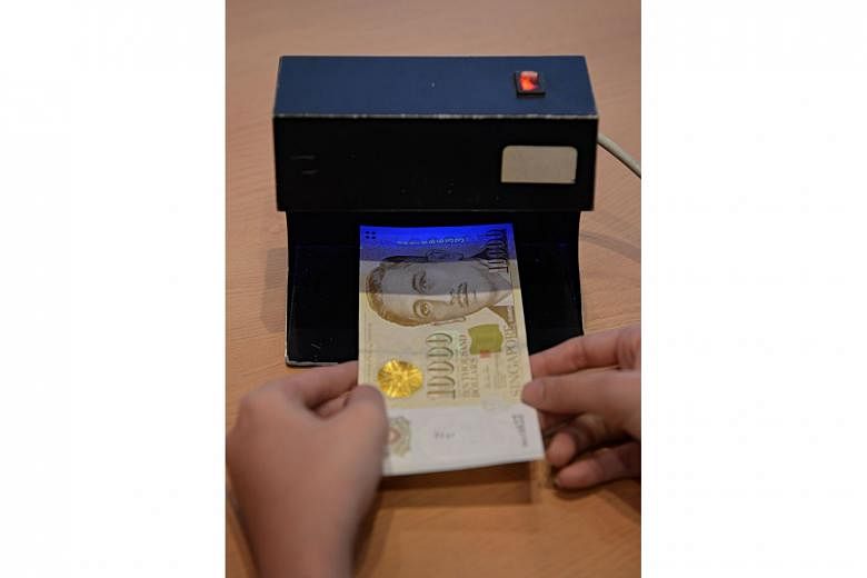 A $10,000 Singapore currency note being examined under a UV scanner. Jusuf Nababan, who pleaded guilty to one count of conspiring with another individual to use a counterfeit note as genuine, was sentenced to four years and two months' jail. ST FILE 