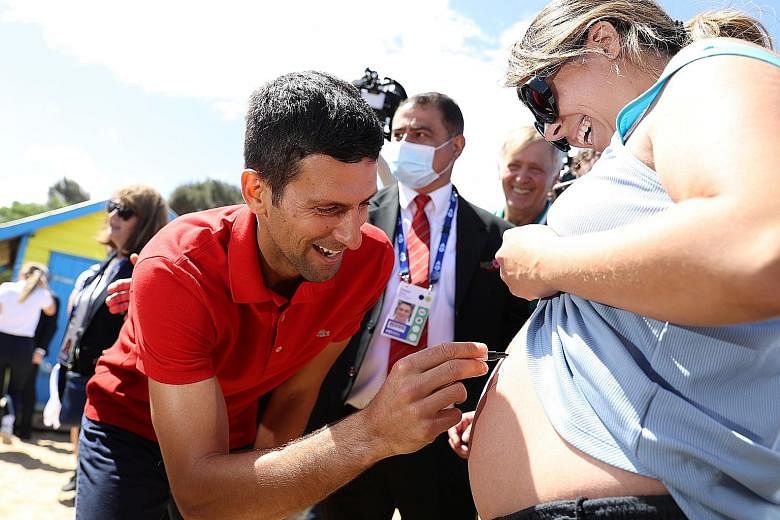 Novak Djokovic signing an expectant mother's belly while parading his Australian Open trophy at Melbourne's Brighton Beach.